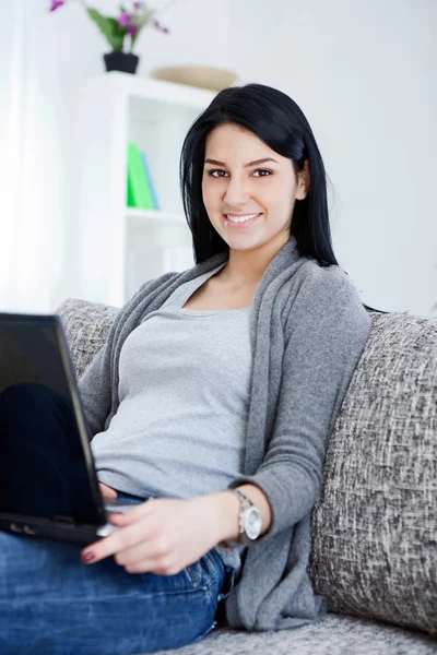 Sorrindo jovem sentada no sofá, usando laptop — Fotografia de Stock