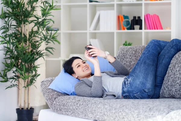 Молода дівчина читає SMS, розслабляючись на дивані — стокове фото