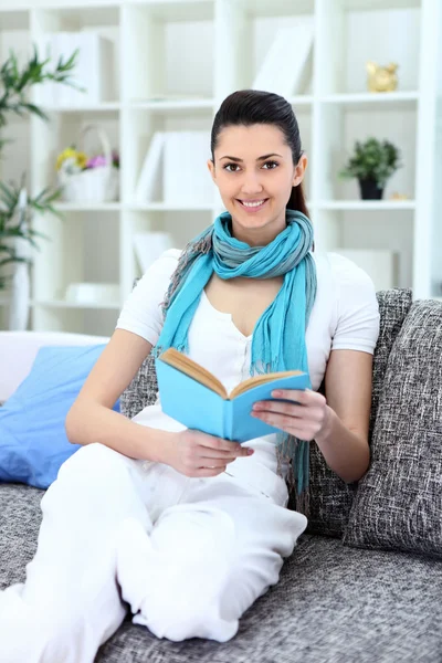 Счастливая молодая женщина сидит на диване с книгой — стоковое фото