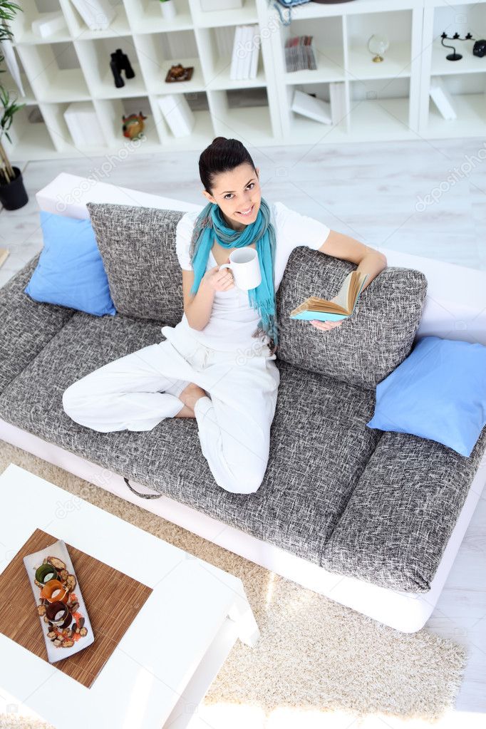 Pretty young woman relaxing on sofa at home and reading book