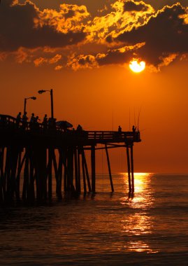 Silhouetted fishermen at sunrise on a fishing pier in North Caro clipart