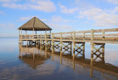 Gazebo, dock, blue sky and clouds over calm sound waters clipart
