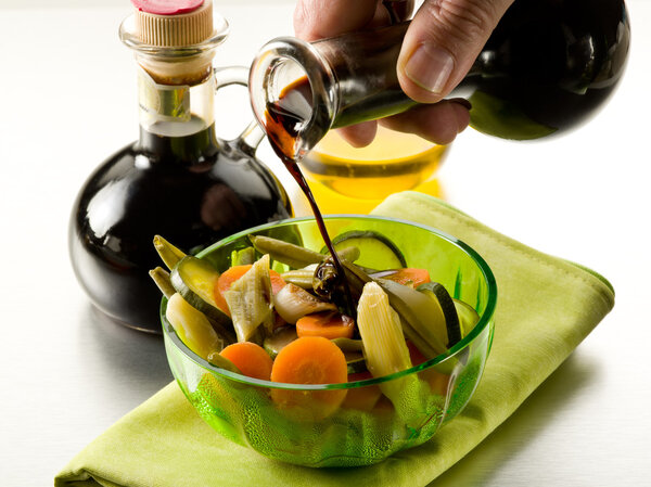 Pouring balsamic vinegar over steamed vegetables salad