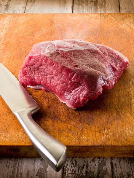 Carne com faca sobre placa de corte — Fotografia de Stock