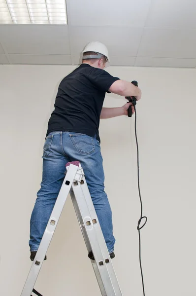 Man på en stege borrar drill — Stockfoto