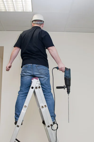 Hombre en una escalera sosteniendo un taladro — Foto de Stock