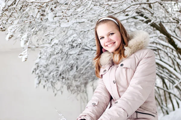 Beautiful young girl in a hood on a background a snow-bound tree — Stock Photo, Image