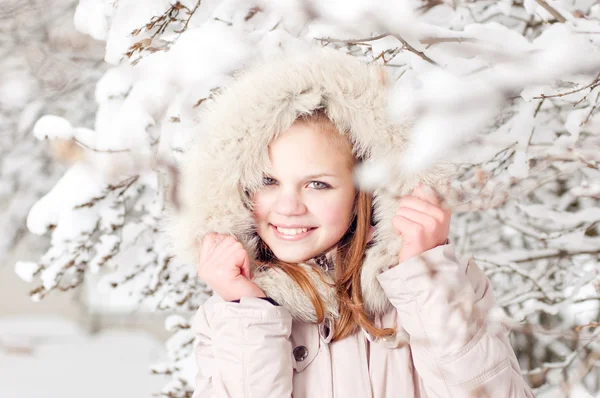 Hermosa joven en una capucha sobre un fondo un árbol nevado — Foto de Stock
