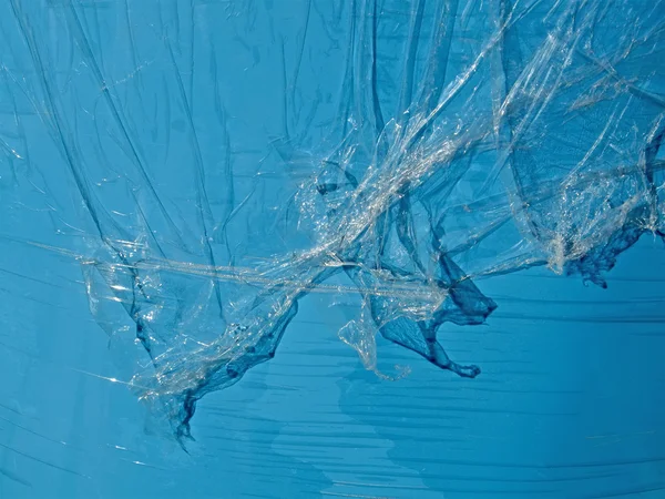 Astratti pezzi di pelle di petrolio plastica trasparente sulla superficie blu . — Foto Stock