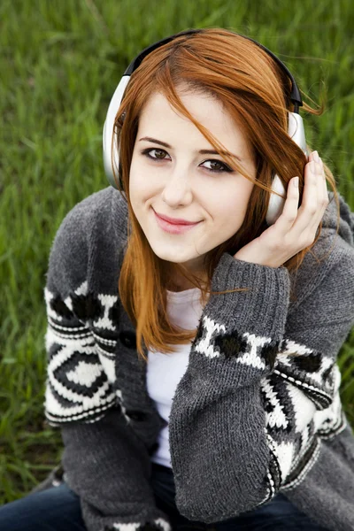 Jonge mode meisje met koptelefoon zitten op groene lente gras — Stockfoto