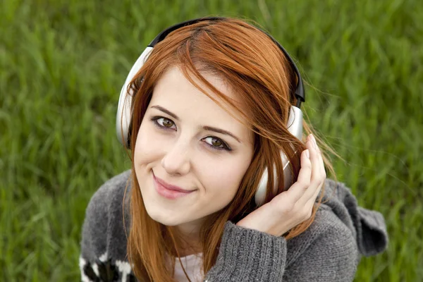 Mladá móda dívka se sluchátky na uších sedí u zelené jarní tráva — Stock fotografie
