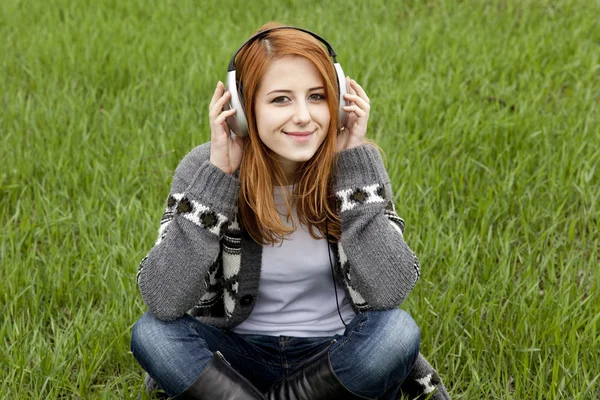 Menina de moda jovem com fones de ouvido sentado na grama de primavera verde — Fotografia de Stock