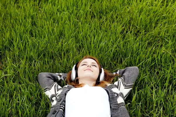 Young fashion girl with headphones lying at green spring grass. — Stock Photo, Image