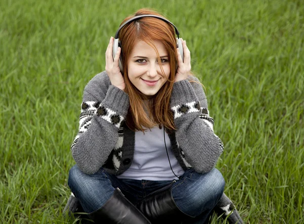 Chica de la moda joven con auriculares sentados en la hierba verde de primavera —  Fotos de Stock