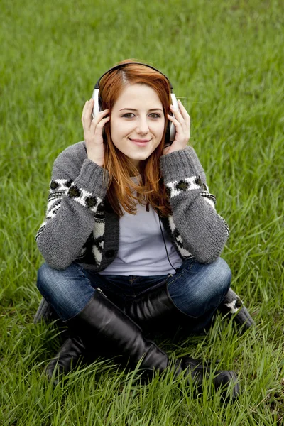 Молодая девушка моды в наушниках сидит на зеленой весенней траве — стоковое фото