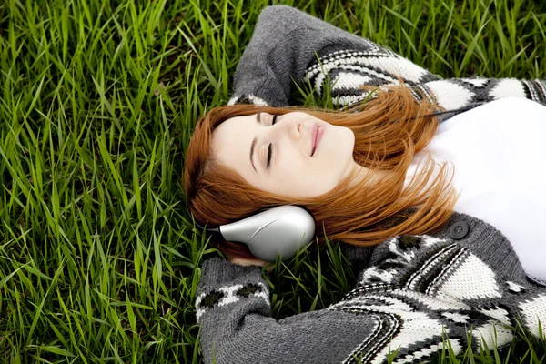 Menina de moda jovem com fones de ouvido deitado na grama de primavera verde . — Fotografia de Stock