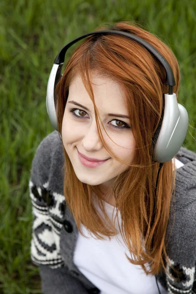 Chica de la moda joven con auriculares sentados en la hierba verde de primavera —  Fotos de Stock
