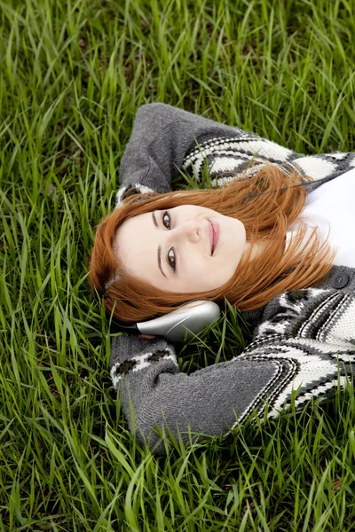 Young fashion girl with headphones lying at green spring grass. — Stock Photo, Image