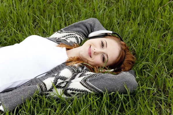 Jeune fille de la mode avec écouteurs couché à l'herbe de printemps vert . — Photo