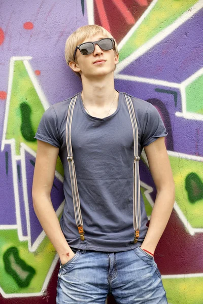 Styl teen chłopiec z w okulary w pobliżu graffiti tło. — Zdjęcie stockowe
