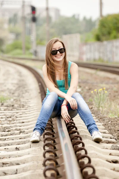 Młoda dziewczyna w okularach siedzący na kolejowej. — Zdjęcie stockowe