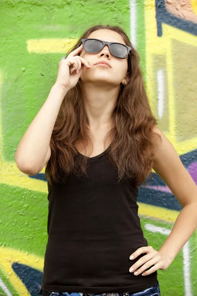Teenager-Mädchen mit Sonnenbrille in der Nähe von Graffiti-Hintergrund. — Stockfoto