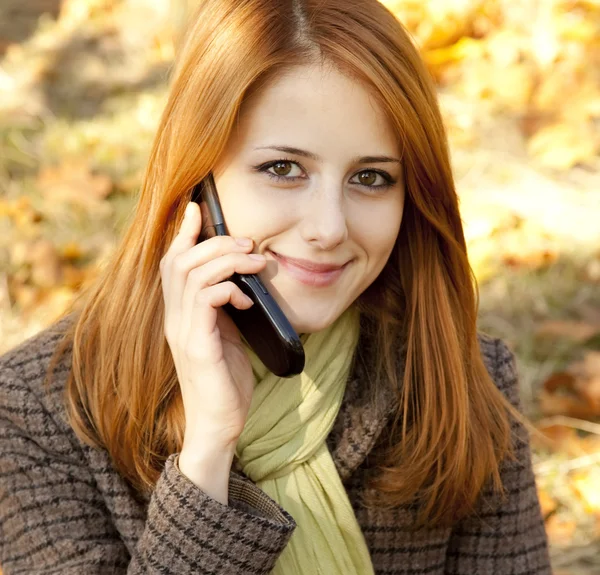Roodharige meisje bellen door de telefoon in de herfst park. — Stockfoto