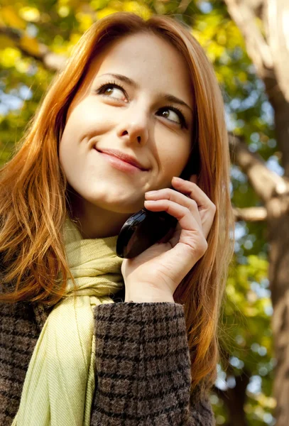 Menina de cabelos vermelhos chamando pelo telefone no parque de outono . — Fotografia de Stock