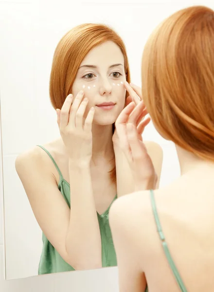 Beautiful redhead young woman with cream on the face in bathroom — Stock Photo, Image