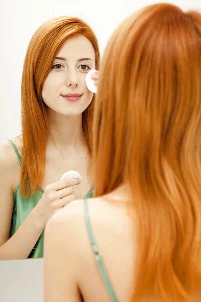 Mooie roodharige jonge vrouw met crème op het gezicht in badkamer — Stockfoto