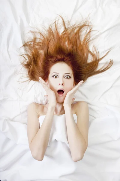 Förvånad rödhåriga flickan i sängen. Studio skott. — Stockfoto