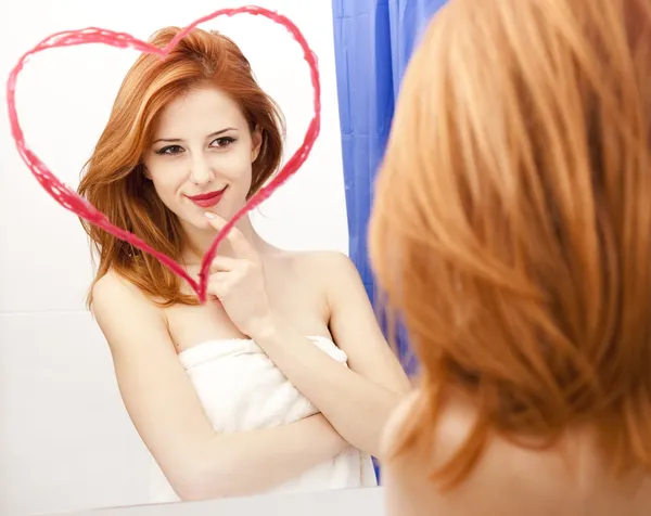 Redhead girl near mirror with heart at it in bathroom. — Stock Photo, Image