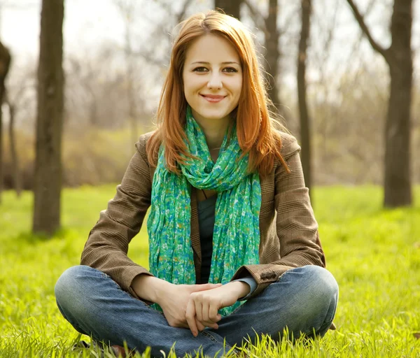 Belle fille aux cheveux roux assise à l'herbe verte au parc . — Photo