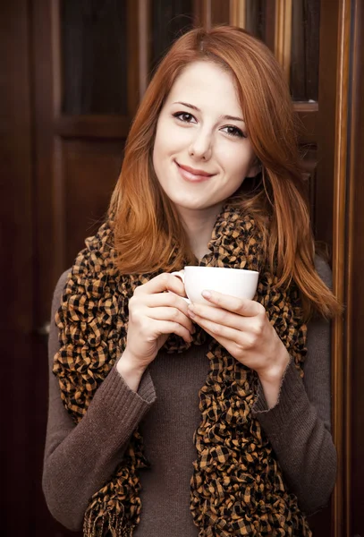 Tyyli punapää tyttö juo kahvia lähellä puu ovet . — kuvapankkivalokuva