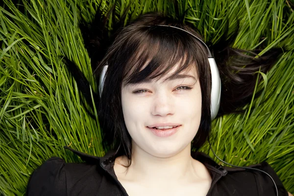 Brunetka dziewczynka słuchania muzyki na zielonej trawie. — Zdjęcie stockowe