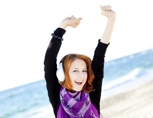 Portrait of red-haired girl in cap with headphone on the beach. — Stock Photo, Image