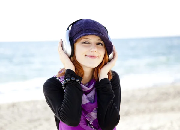 Portrait of red-haired girl in cap with headphone on the beach. — Stock Photo, Image