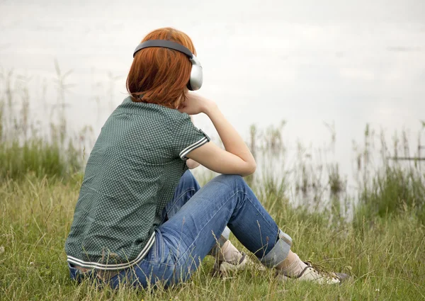 Chica de la moda joven con auriculares en la hierba cerca del lago en primavera —  Fotos de Stock