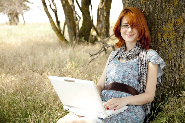 안경 및 노트북 근처에 앉아 있는 젊은 웃는 패션 소녀 — 스톡 사진