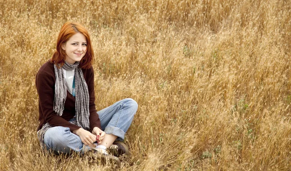 Vacker rödhårig flicka sitter vid gula höst gräset. — Stockfoto