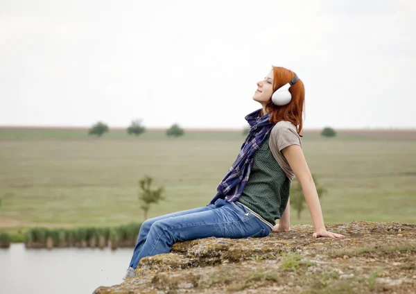 Young fashion girl with headphones at rock near lake. Stock Picture