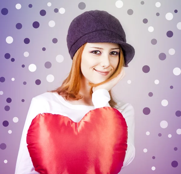 Beautiful red-haired girl in cap with toy heart. — Stock Photo, Image