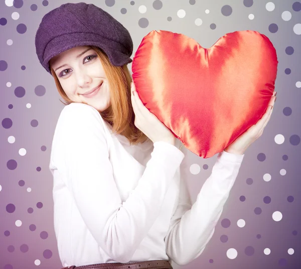 Beautiful red-haired girl in cap with toy heart. — Stock Photo, Image