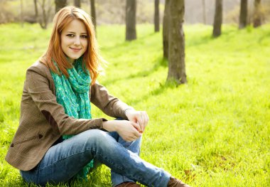 yeşil çimen parkta oturan güzel kızıl saçlı kız.