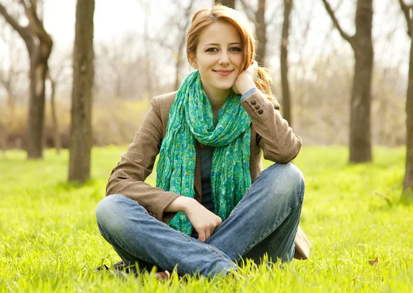 公園の緑の芝生に座って美しい赤い髪の少女. — ストック写真