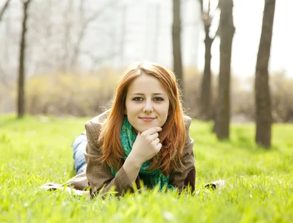 Menina ruiva bonita sentada na grama verde no parque . — Fotografia de Stock