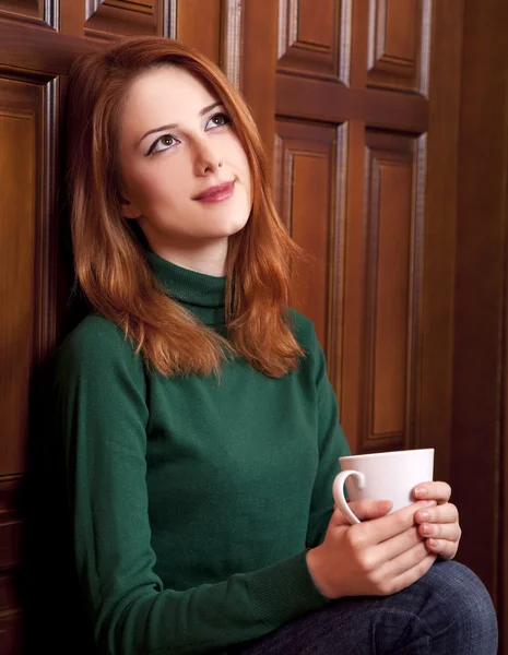 Stile ragazza rossa bere caffè vicino a porte di legno . — Foto Stock