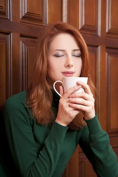 Estilo chica pelirroja beber café cerca de puertas de madera . —  Fotos de Stock