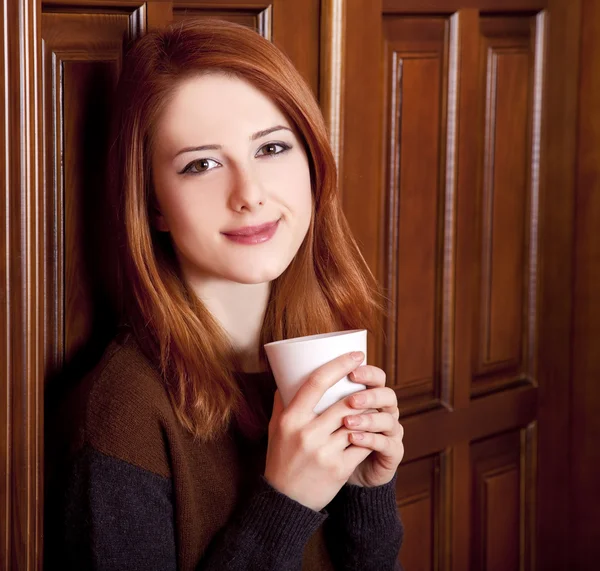 Estilo chica pelirroja beber café cerca de puertas de madera . — Foto de Stock