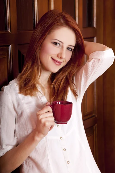 Style redhead girl drinking coffee near wood doors. — Stock Photo, Image